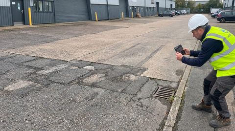 Surveyor recording the condition of a kerb and asphalt surface on a commercial estate