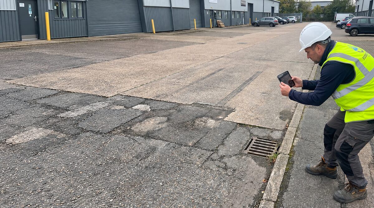 Surveyor recording the condition of a kerb and asphalt surface on a commercial estate