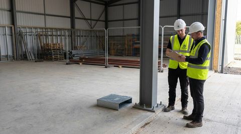 Site team reviewing a drawing beside a steel column base inside a warehouse shell